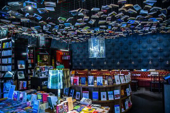 Intérieur d'une grandiose librairie avec des livres suspendus au plafond et des sièges confortables dans une atmosphère magique.