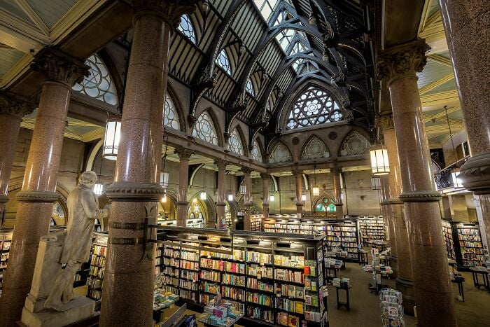Intérieur grandiose de bibliothèque avec de hautes colonnes, des plafonds voûtés et des étagères remplies de livres dans un cadre magique.
