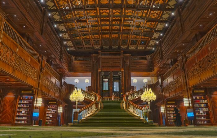 Intérieur grandiose d'une bibliothèque avec un grand escalier, des murs en bois ornés et des étagères remplies de livres dans un cadre magique.