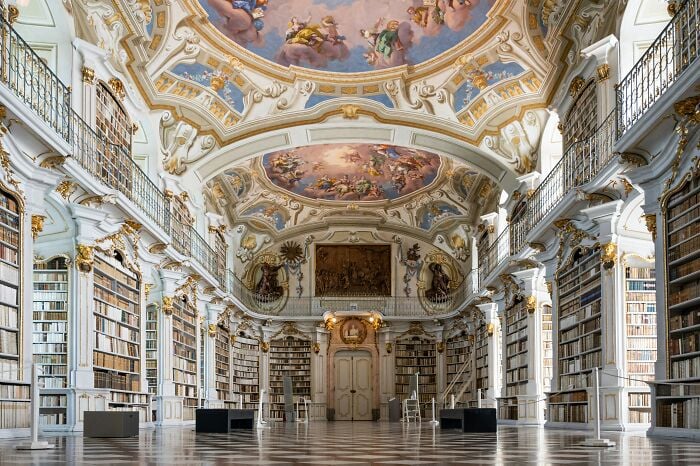 Interno grandioso di una biblioteca con soffitti ornati e alte scaffalature piene di libri in un'atmosfera magica.