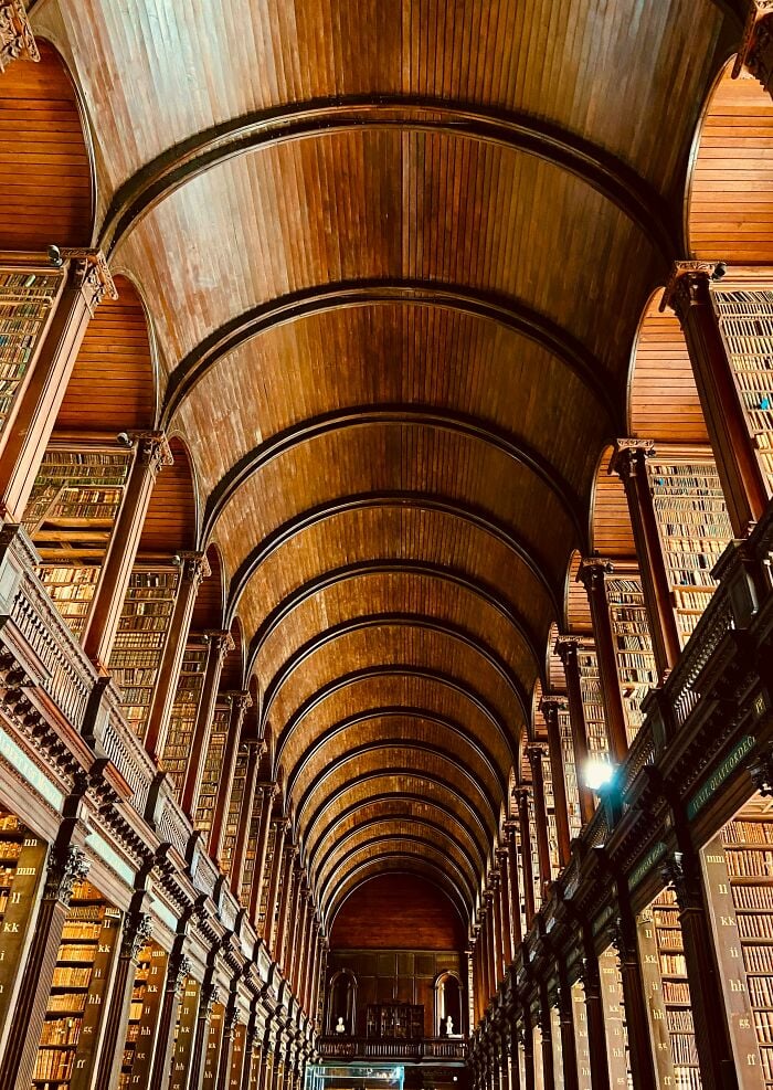 Interior grandioso de biblioteca con techo abovedado de madera alto y estanterías altas llenas de libros de suelo a techo.