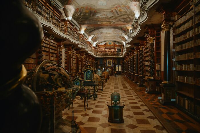Grandiose library interior with antique globes, ornate columns, and rows of old books on wooden shelves. Grandiose library interior with antique globes, ornate columns, and rows of old books on wooden shelves.